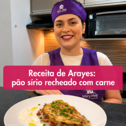 Profissional da Mary Help sorrindo em uma cozinha, ao lado de um prato de Arayes, pão sírio recheado com carne, acompanhado de molho cremoso. A imagem apresenta uma receita de Arayes de carne.