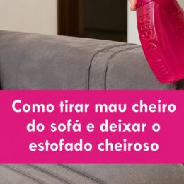 Mão borrifando uma solução de limpeza em um sofá cinza, com o texto “Como tirar mau cheiro do sofá e deixar o estofado cheiroso” em destaque.